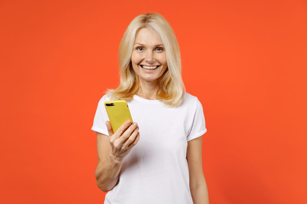 femme de 65 ans souriant devant son smartphone en cherchant une mutuelle sénior