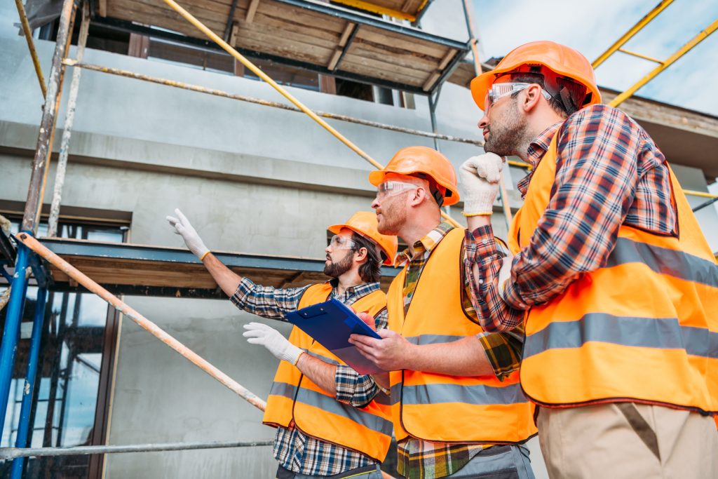 ouvriers avec casque et gilets orange regardant un bâtiment