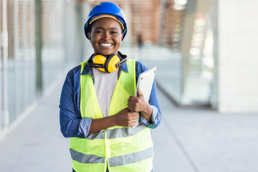 Ouvrière souriante avec casque bleu et gilet jaune et une tablette numérique