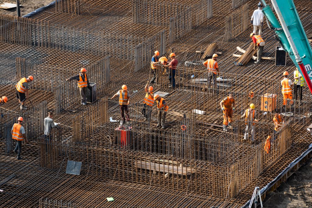 une dizaine d'ouvriers vêtus de gilets et de casques orange faisant les fondation d'un gros bâtiment